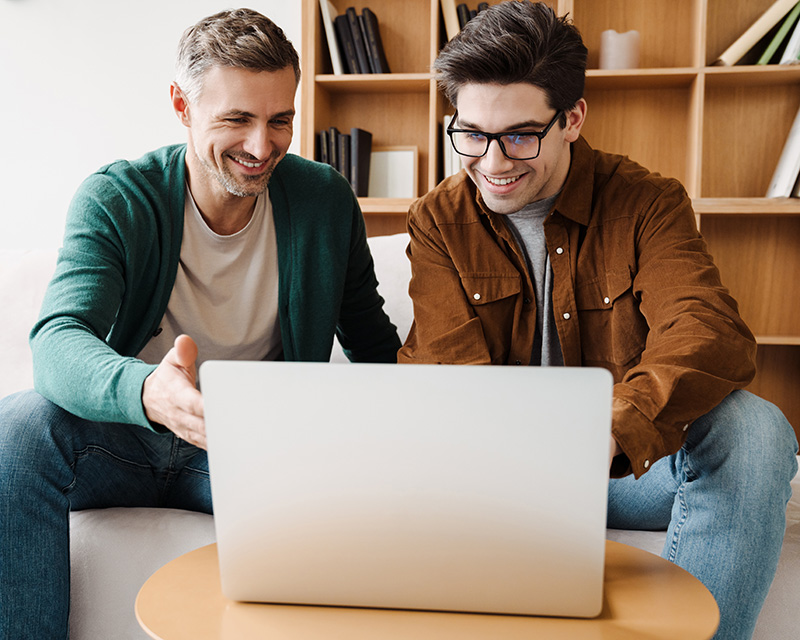 Gay couple on a couch in front of a laptop for online couples counseling in New York