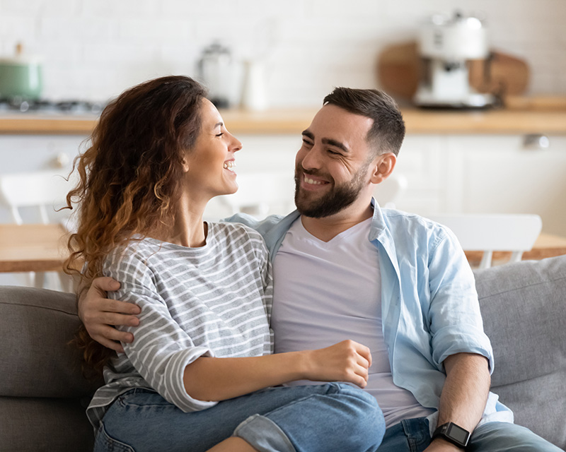 Couple sitting on the couch smiling at one another. Online couples therapy in NY