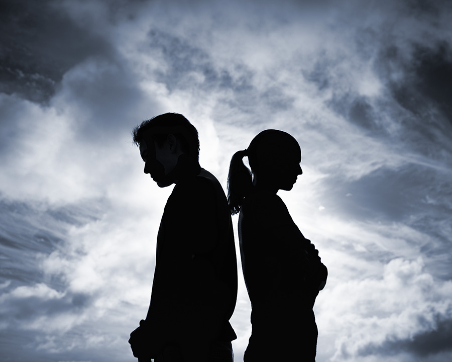 Couple in silhouette standing back to back with clouds. In need of discernment counseling to determine if relationship should go forward